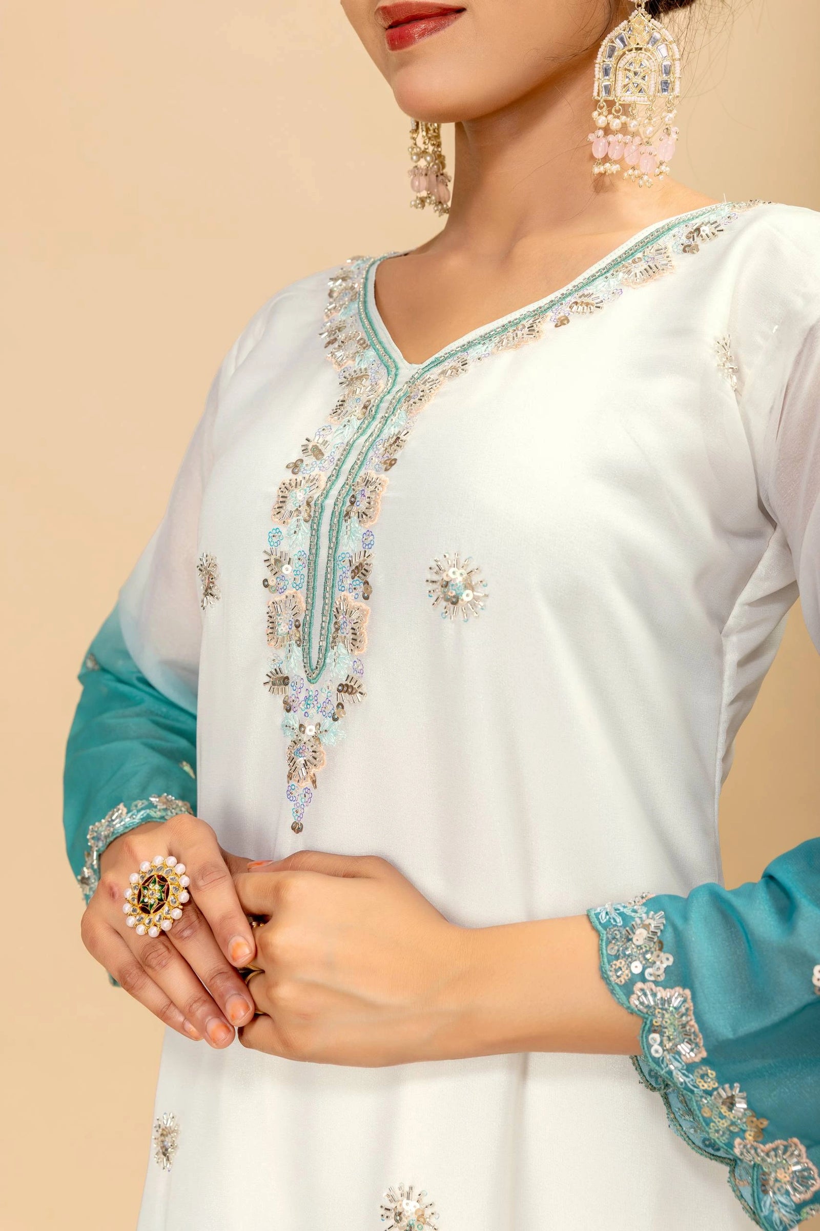 White outfit with blue embroidery and jewelry on a beige background