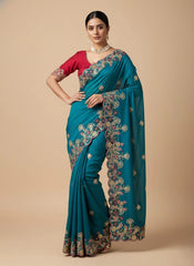 Woman wearing a teal saree with intricate patterns on a beige background