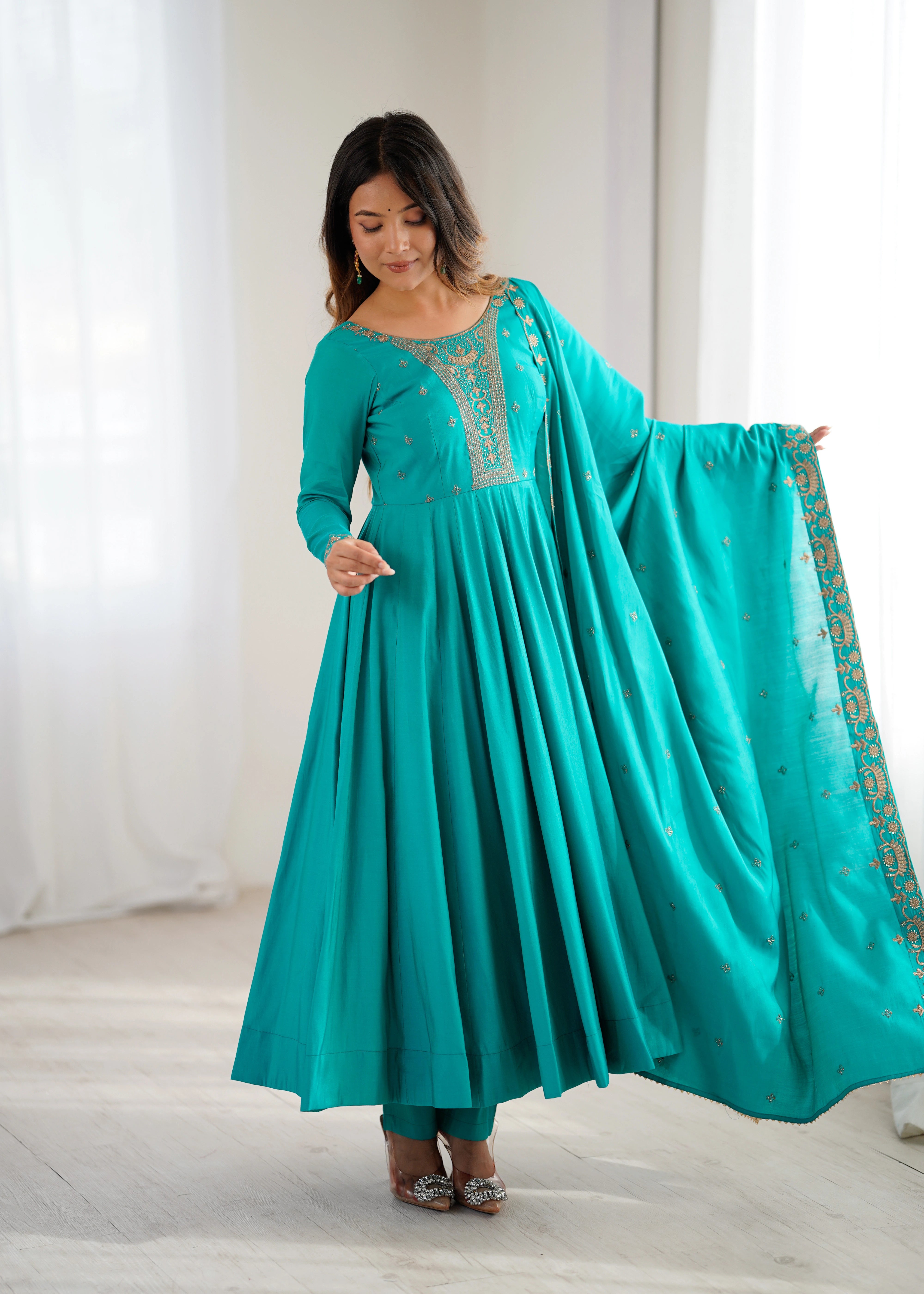 Woman wearing a teal traditional outfit with a matching dupatta in a bright room.