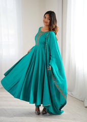 Woman wearing a teal traditional outfit with a matching dupatta against a white curtain background