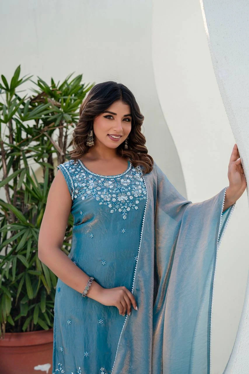 Woman in a blue embroidered dress standing outdoors with a plant in the background