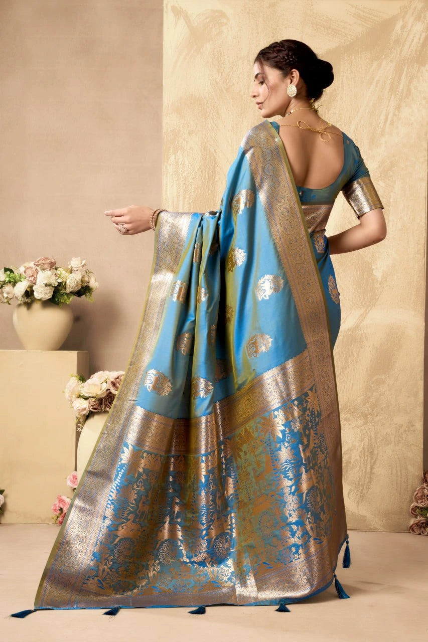 Woman wearing a traditional saree with a blue and gold pattern, standing against a beige wall.