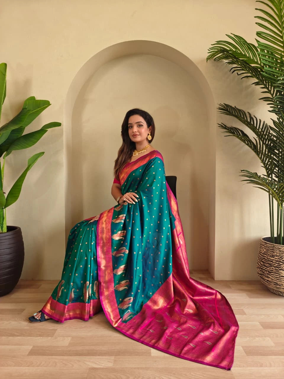 Woman in a teal and pink saree standing in a room with plants.