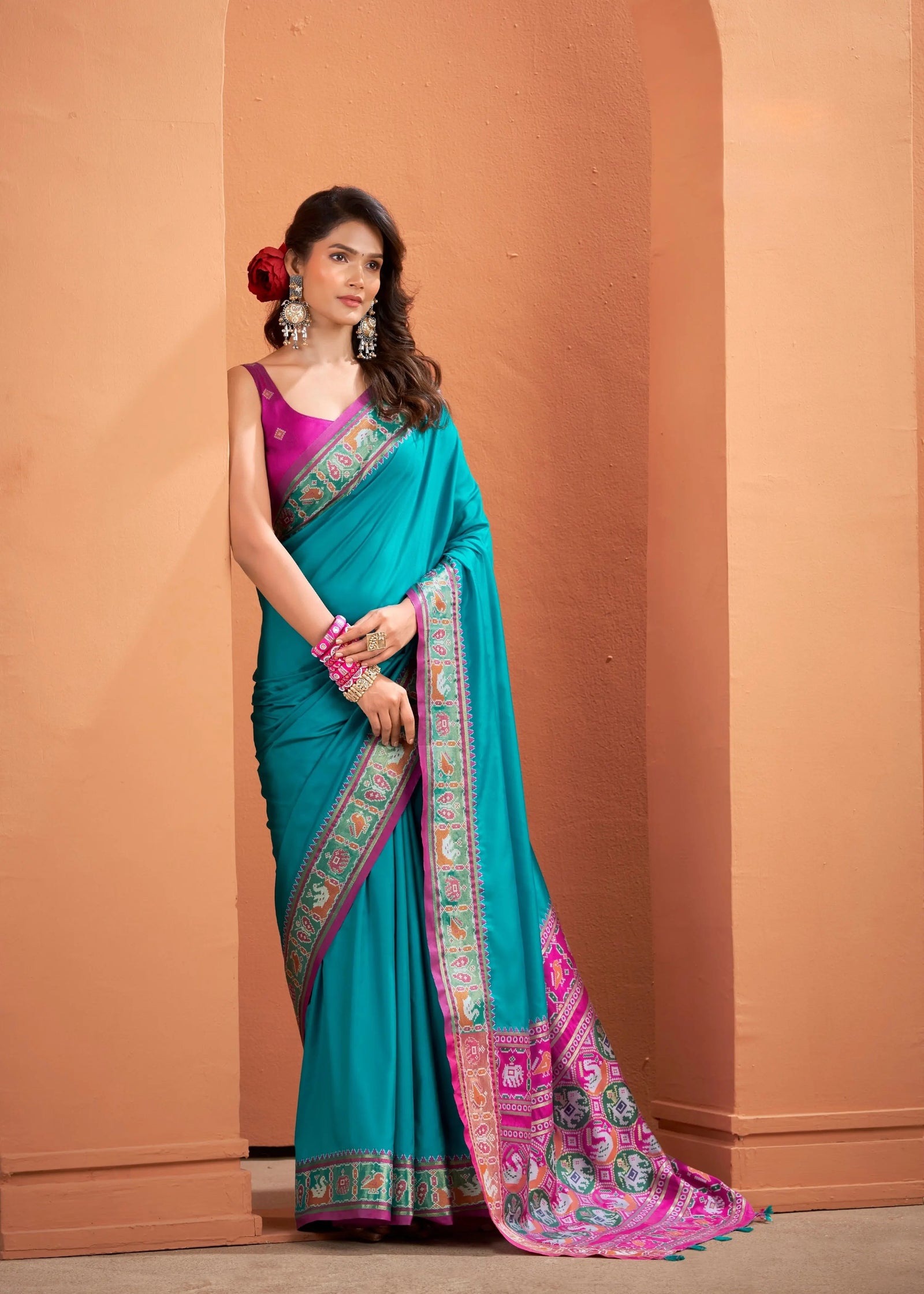 Woman wearing a teal and pink saree against a beige wall