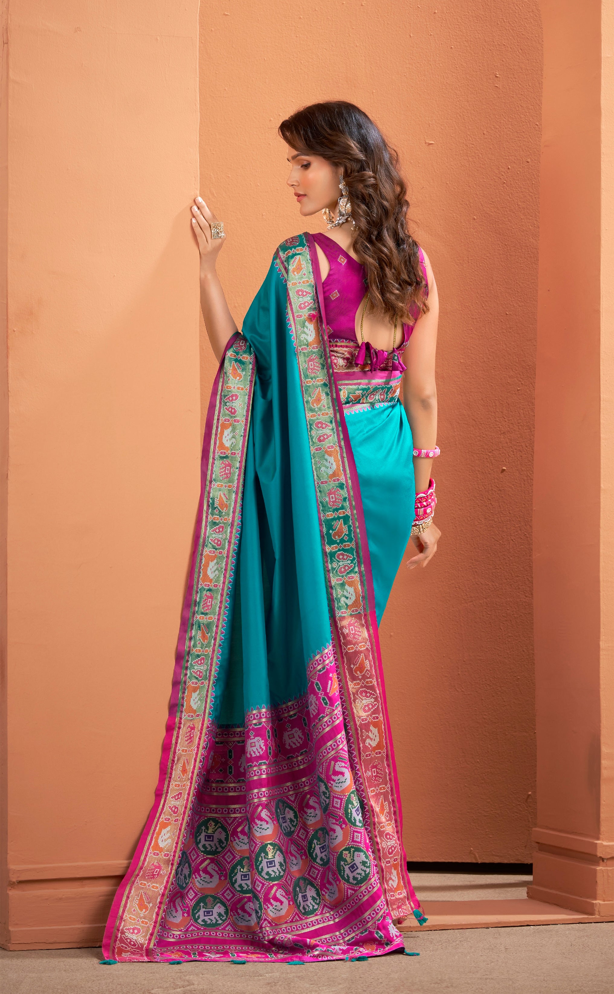 Woman wearing a vibrant turquoise and pink saree with a plain background