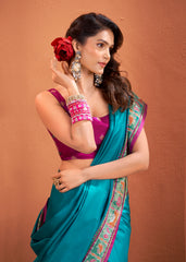 Woman wearing a blue saree with a purple blouse, holding a red flower against a brown background