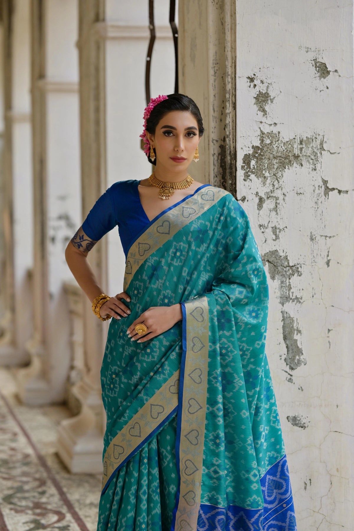 Woman wearing a teal saree with a blue blouse in an indoor setting.