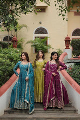 Three women in traditional dresses standing on steps with a building and greenery in the background