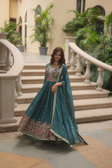 Woman in a teal traditional outfit standing on steps with greenery in the background