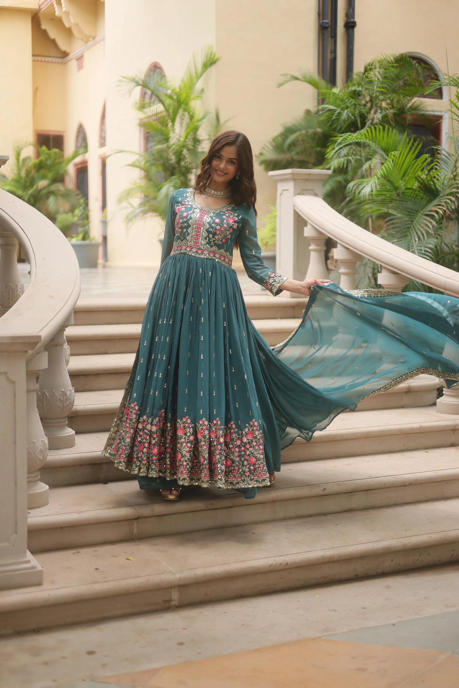 Woman in a teal dress with floral patterns standing on stone steps outdoors.