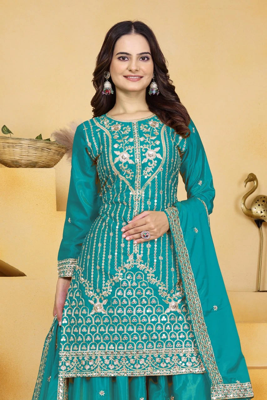 Woman wearing a teal embroidered traditional outfit with a beige background