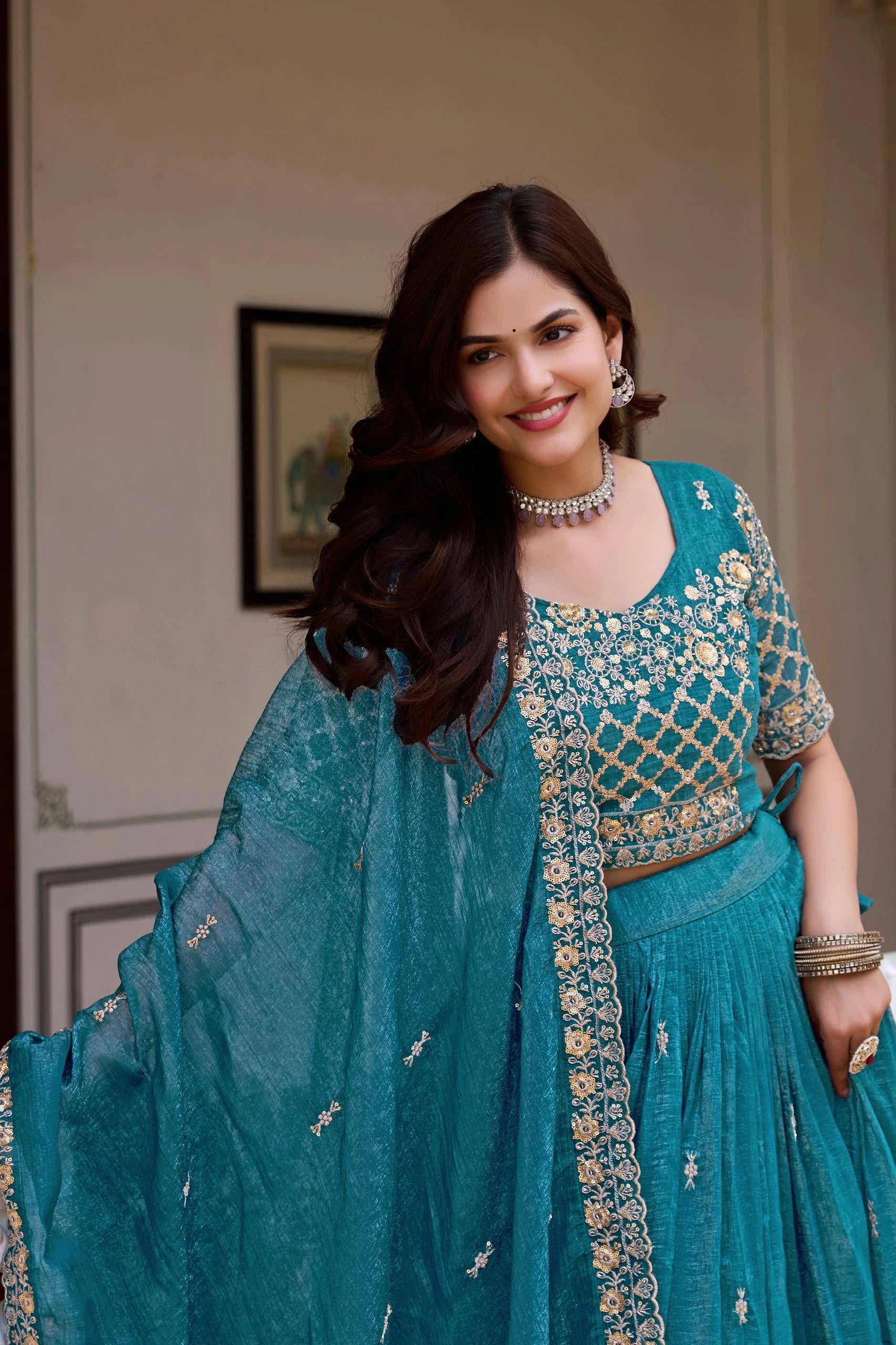 Woman in a teal traditional outfit with intricate patterns indoors.