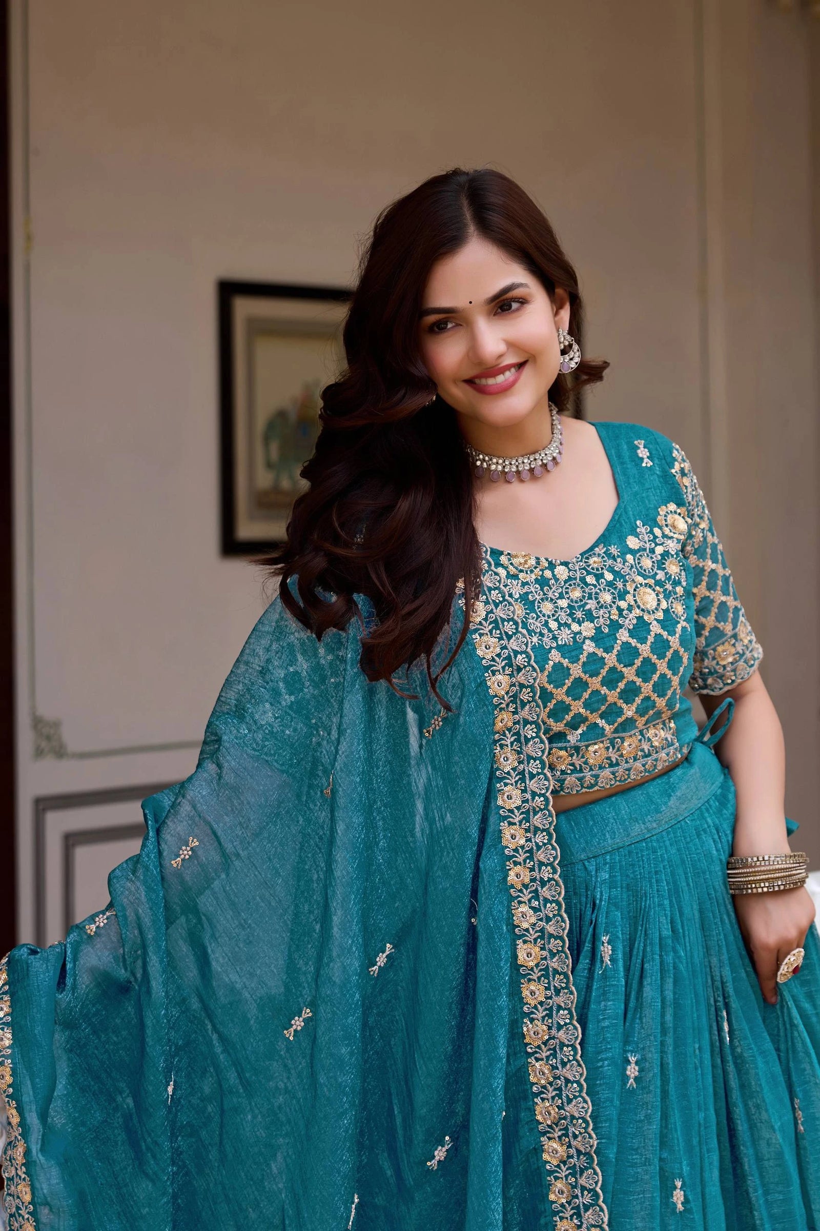 Woman in a teal traditional outfit with intricate patterns indoors.
