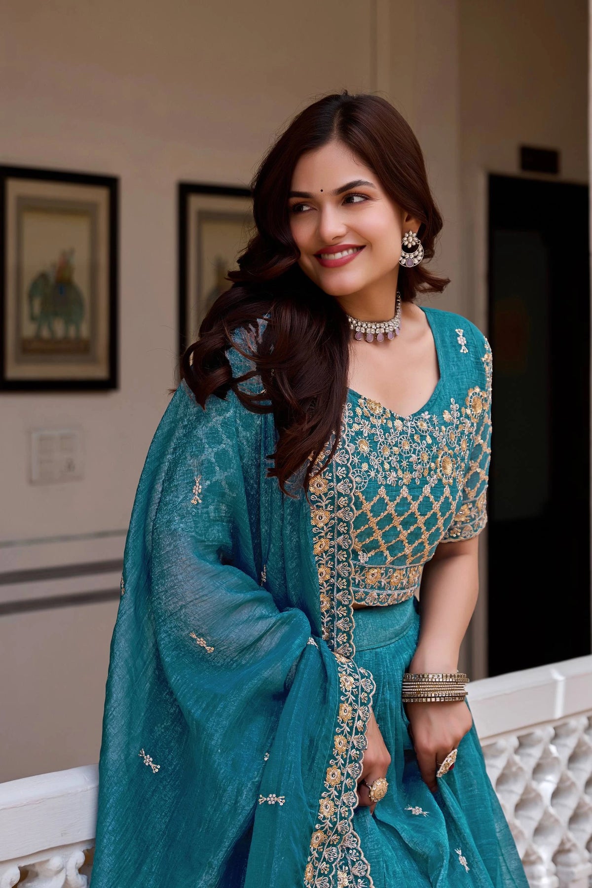 Woman in a teal traditional outfit with gold embroidery indoors.