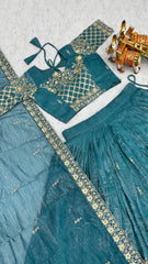 Teal traditional outfit with gold embroidery on a textured surface
