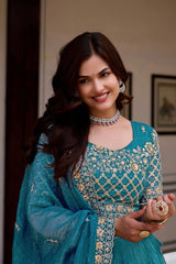 Woman in a blue embroidered traditional outfit with jewelry indoors.