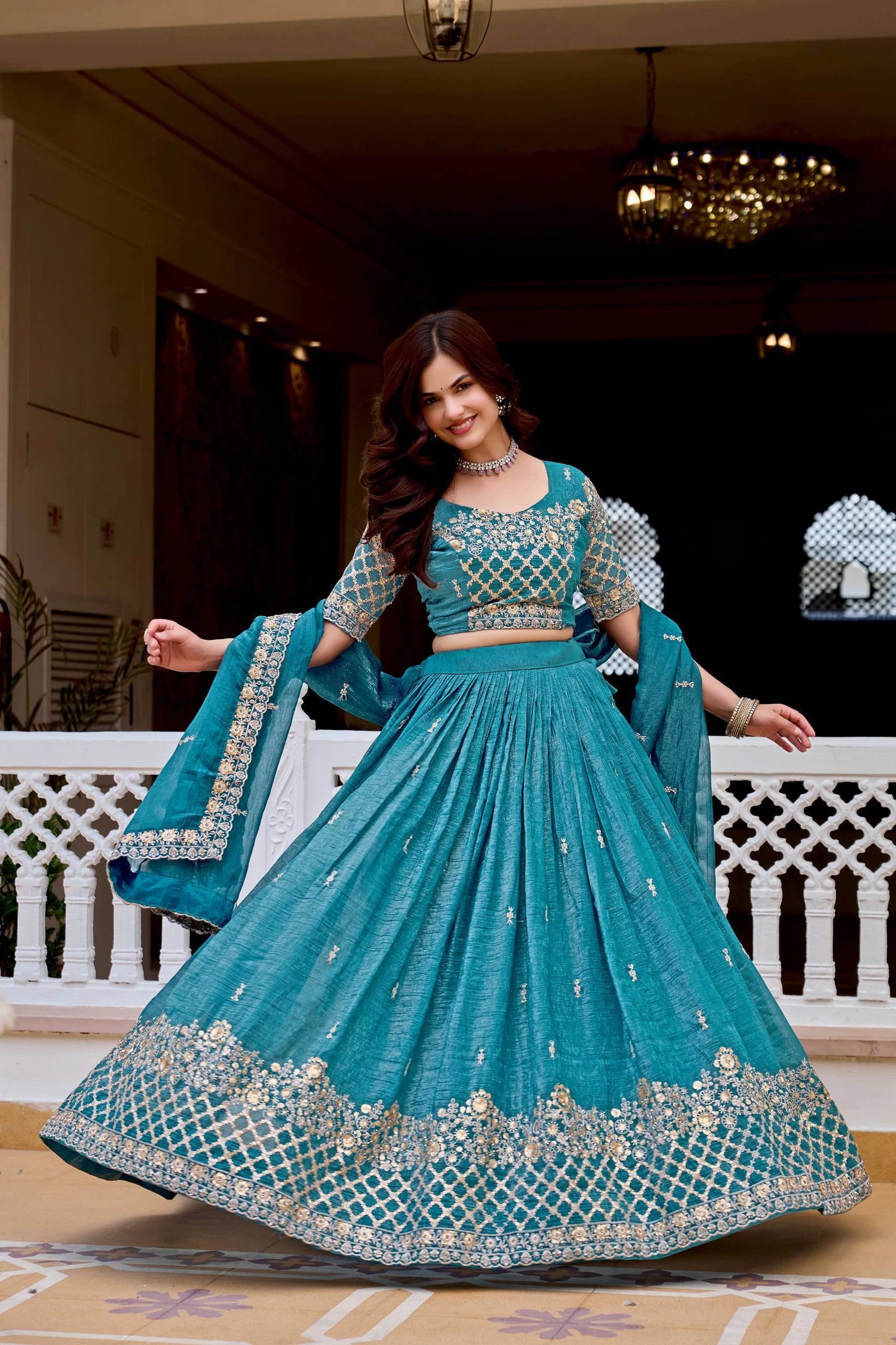 Woman in a traditional teal outfit with silver embroidery on a decorative floor.