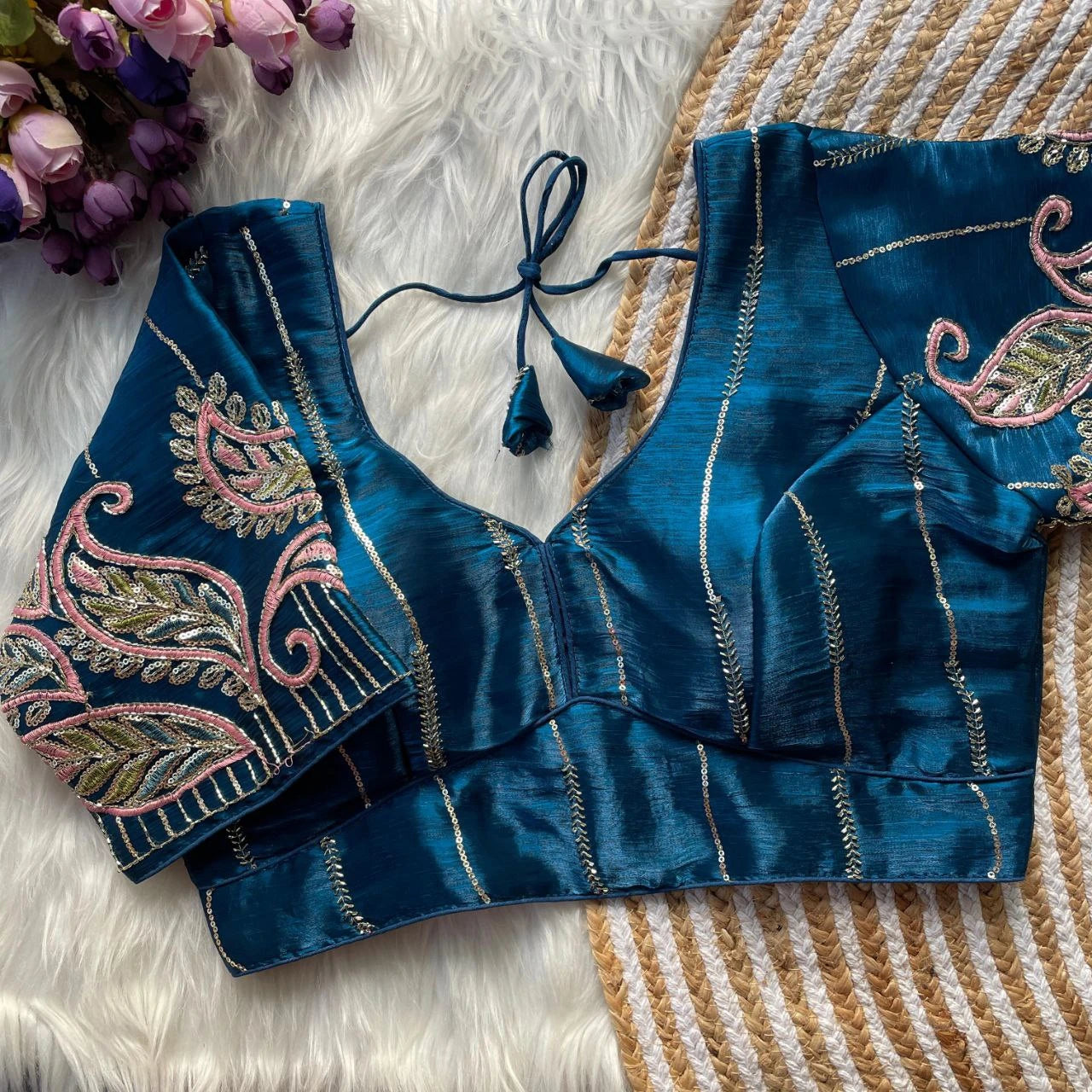 Blue embroidered blouse with floral patterns on a textured surface with flowers.