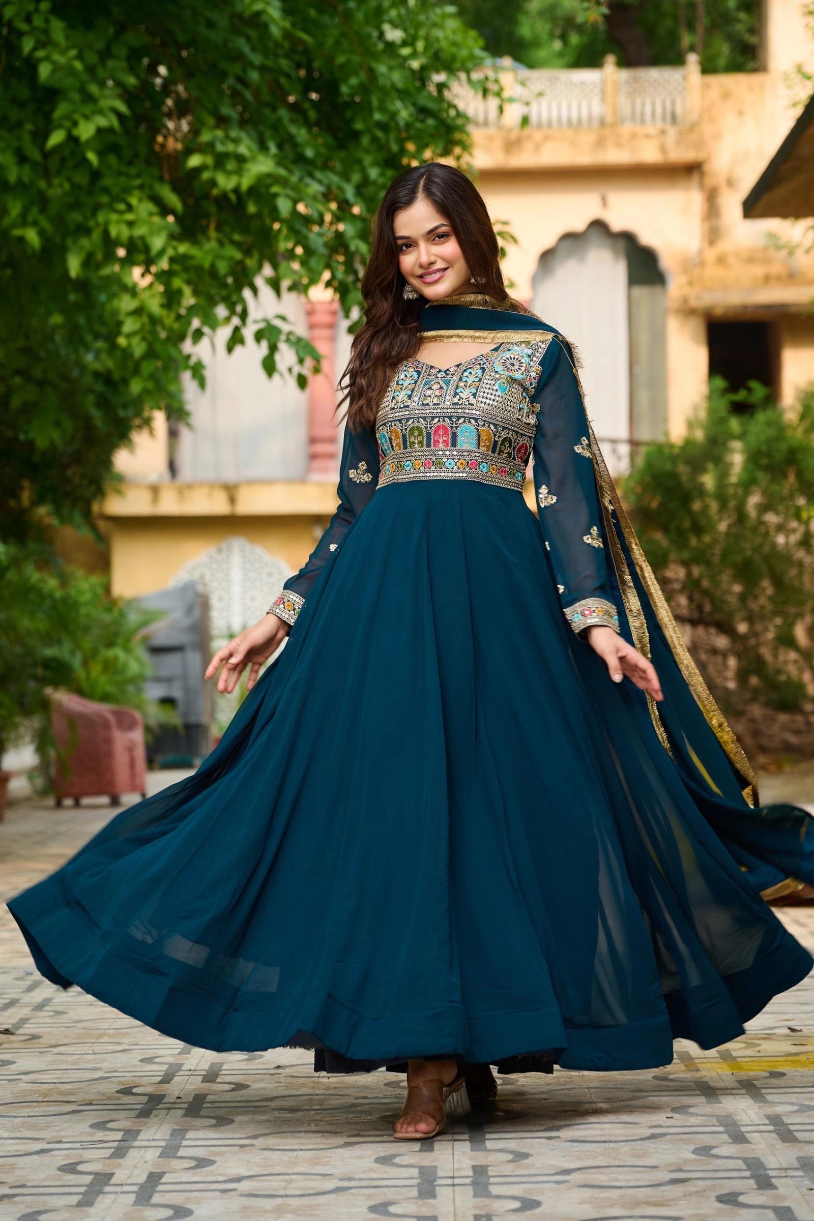 Woman in a blue traditional outfit with intricate patterns standing outdoors.