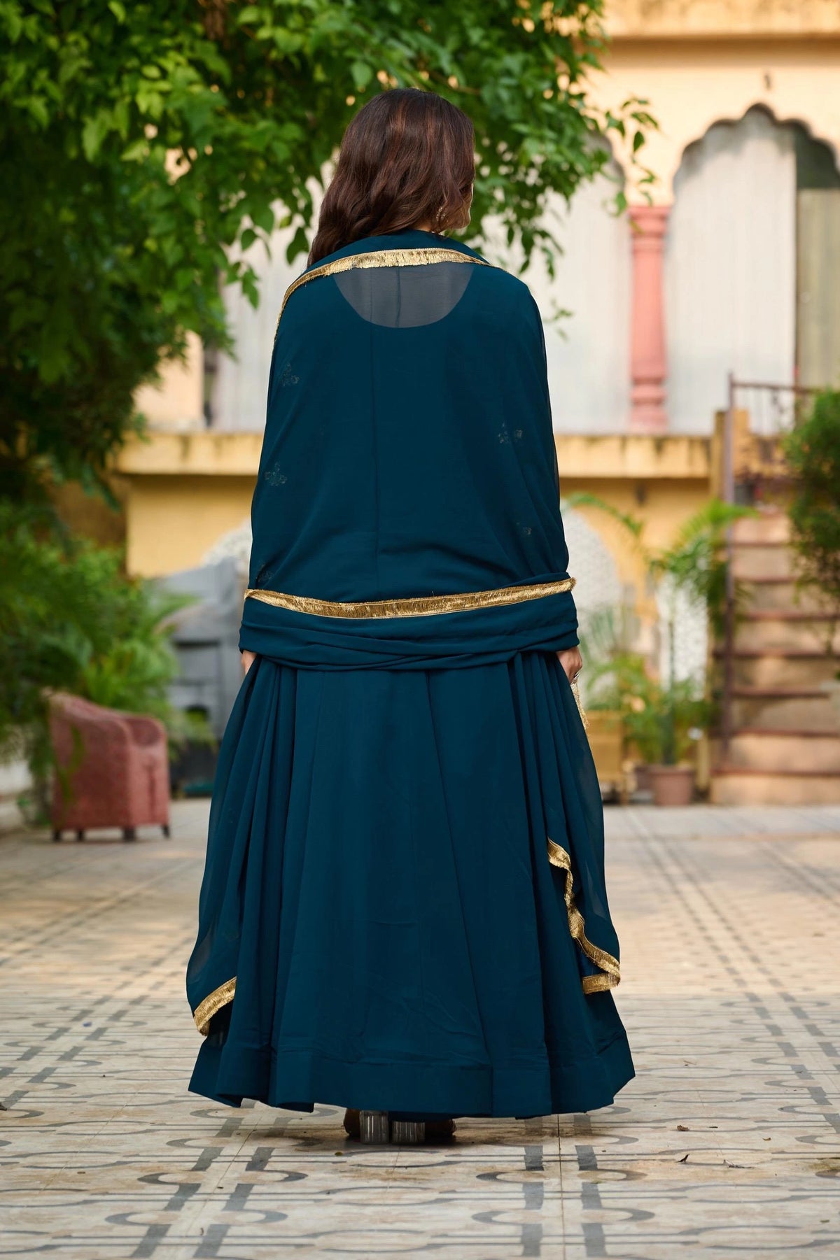 Person wearing a teal dress with gold accents in an outdoor setting