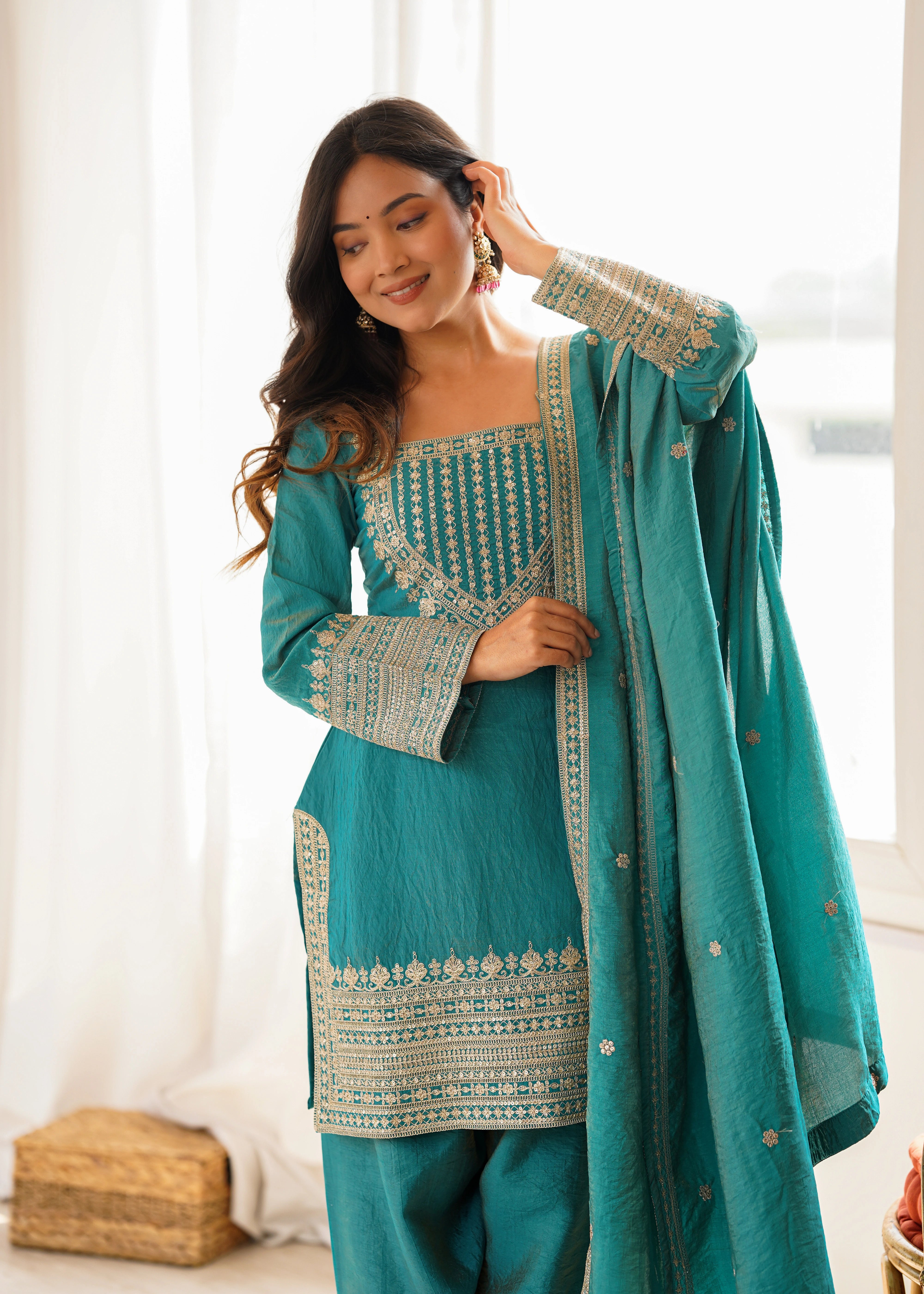 Woman wearing a teal traditional outfit with white embroidery indoors.