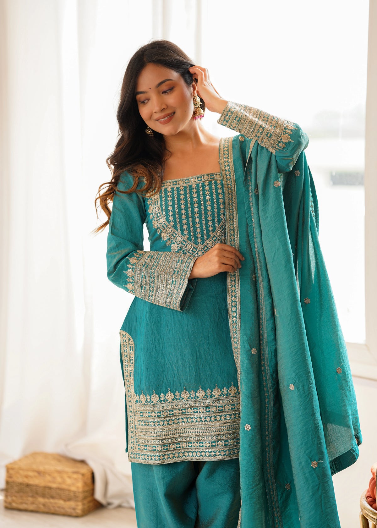 Woman wearing a teal traditional outfit with white embroidery indoors.