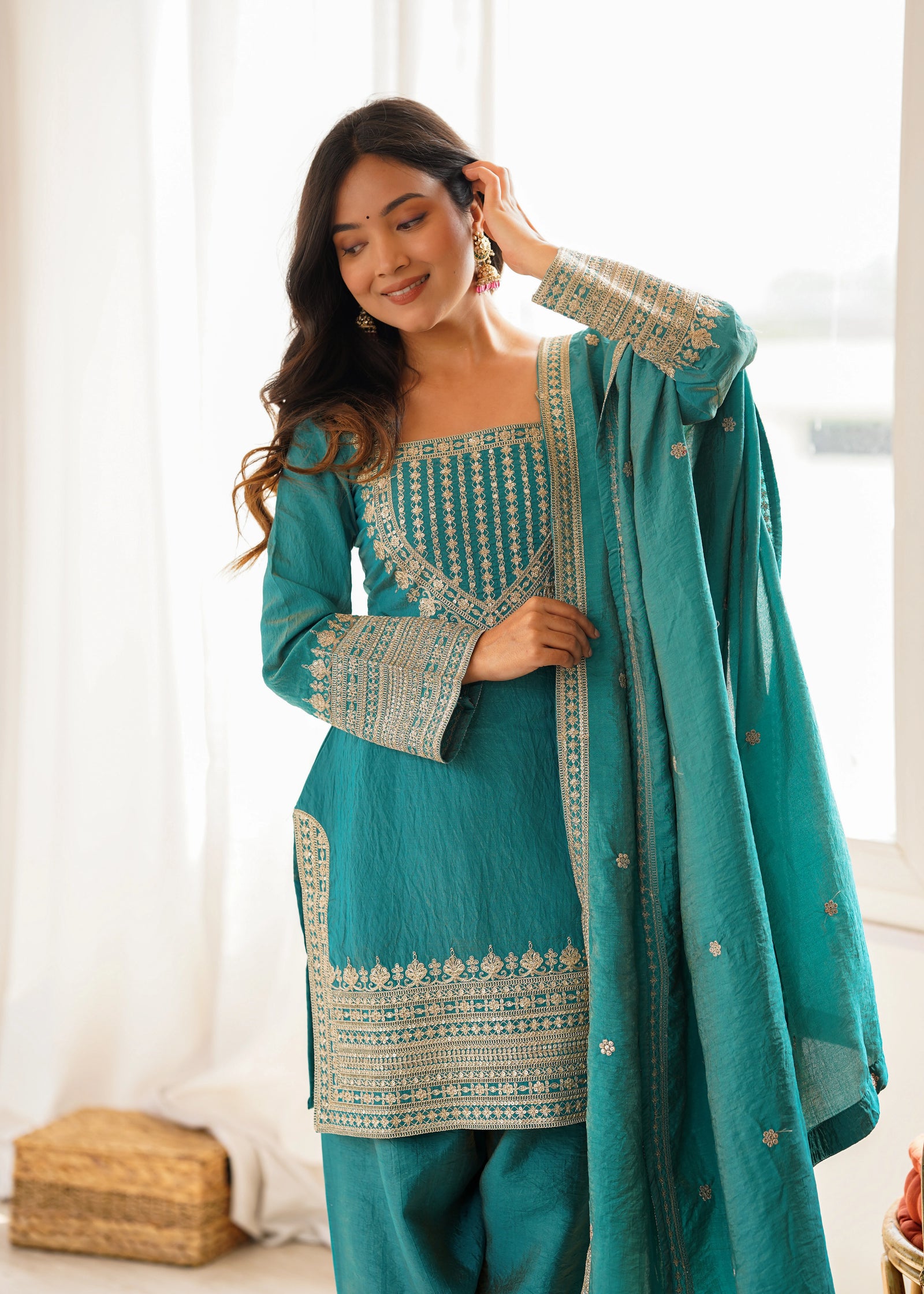 Woman wearing a teal traditional outfit with white embroidery indoors.