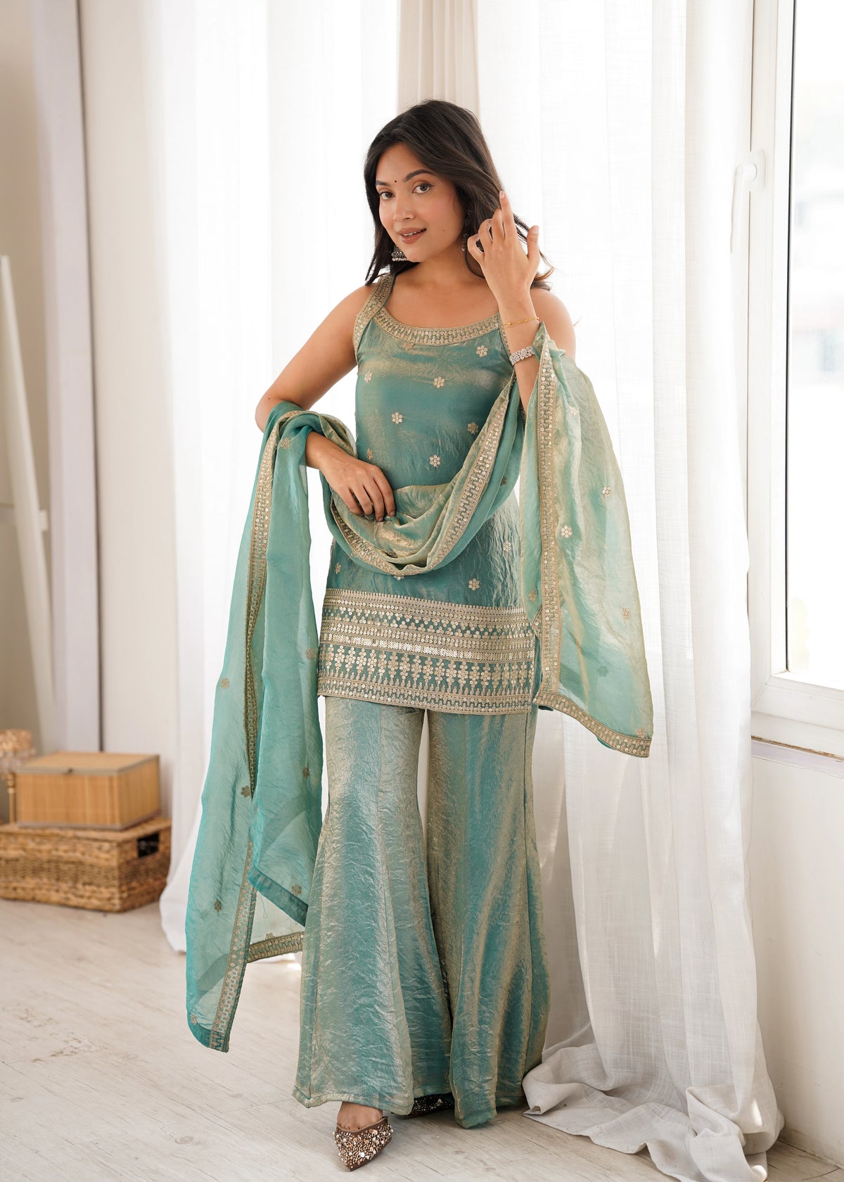 Woman in a teal traditional outfit with a matching dupatta in a bright room.