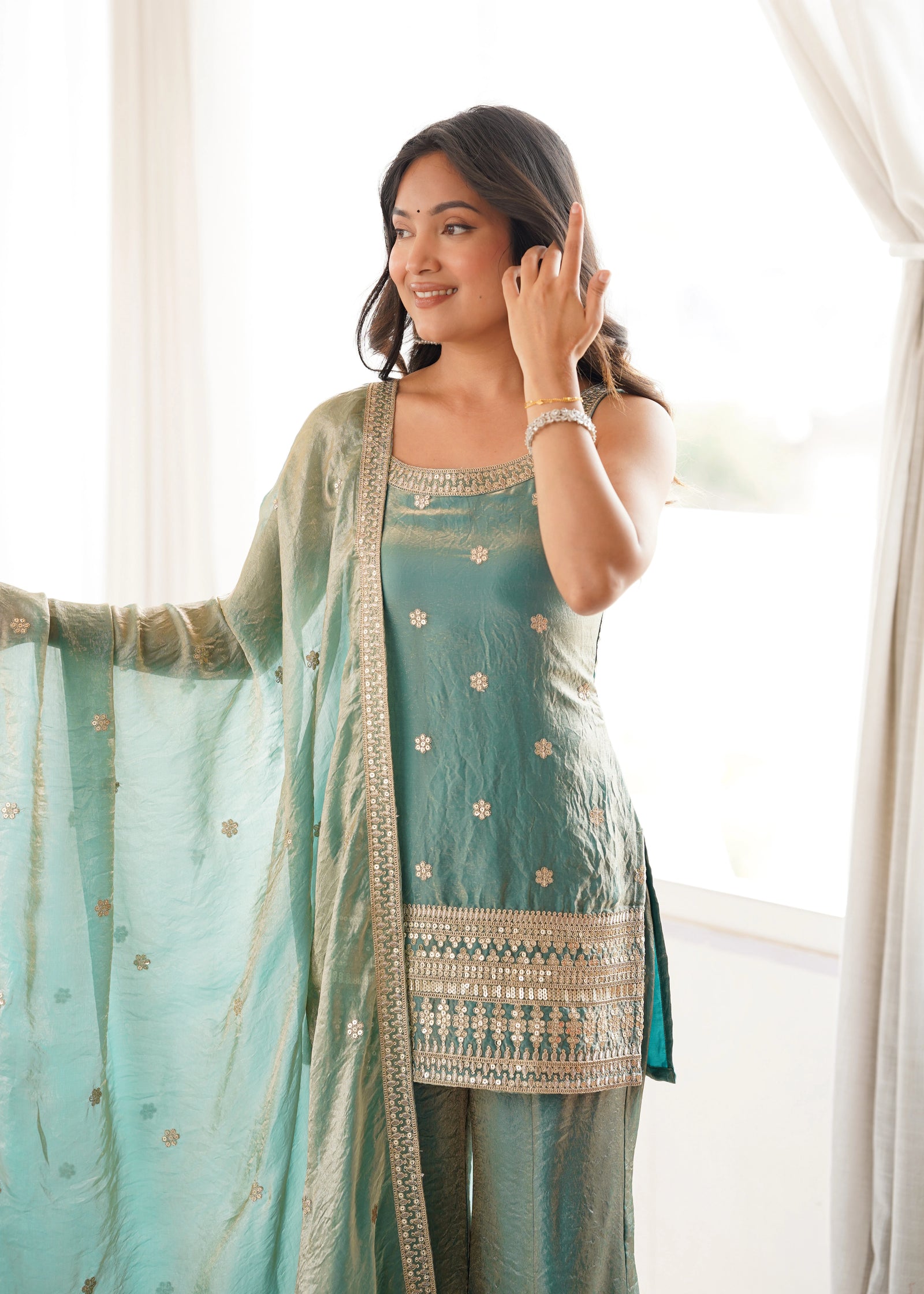 Woman wearing a light blue traditional outfit with a matching dupatta, standing indoors.