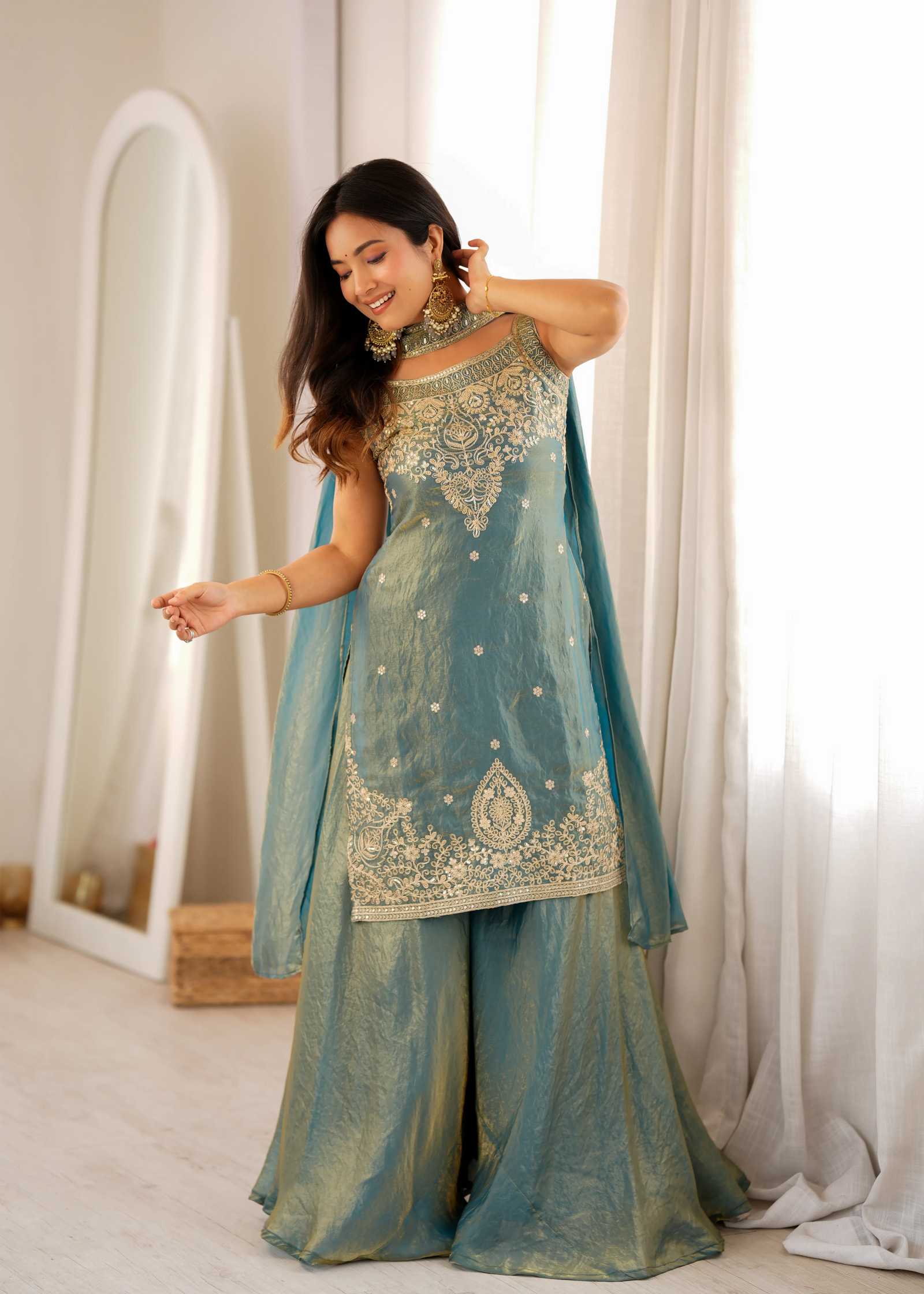 Woman in a traditional outfit with intricate designs in a bright room.