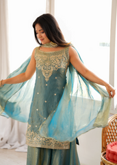 Woman wearing a teal traditional outfit with gold embroidery in a bright room.