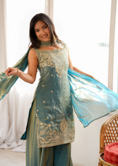 Woman wearing a traditional outfit with a blue and green color scheme indoors.