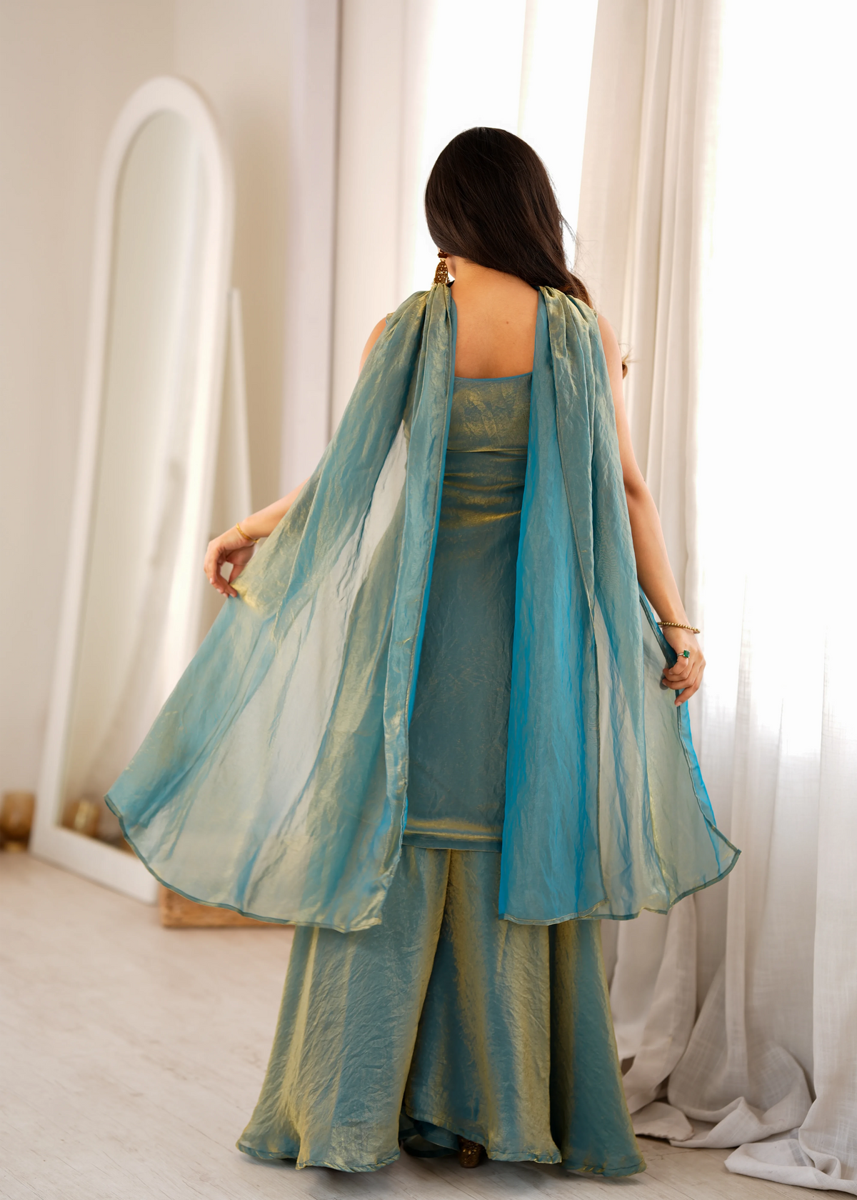 Woman wearing a teal traditional outfit with a matching dupatta in a bright room.