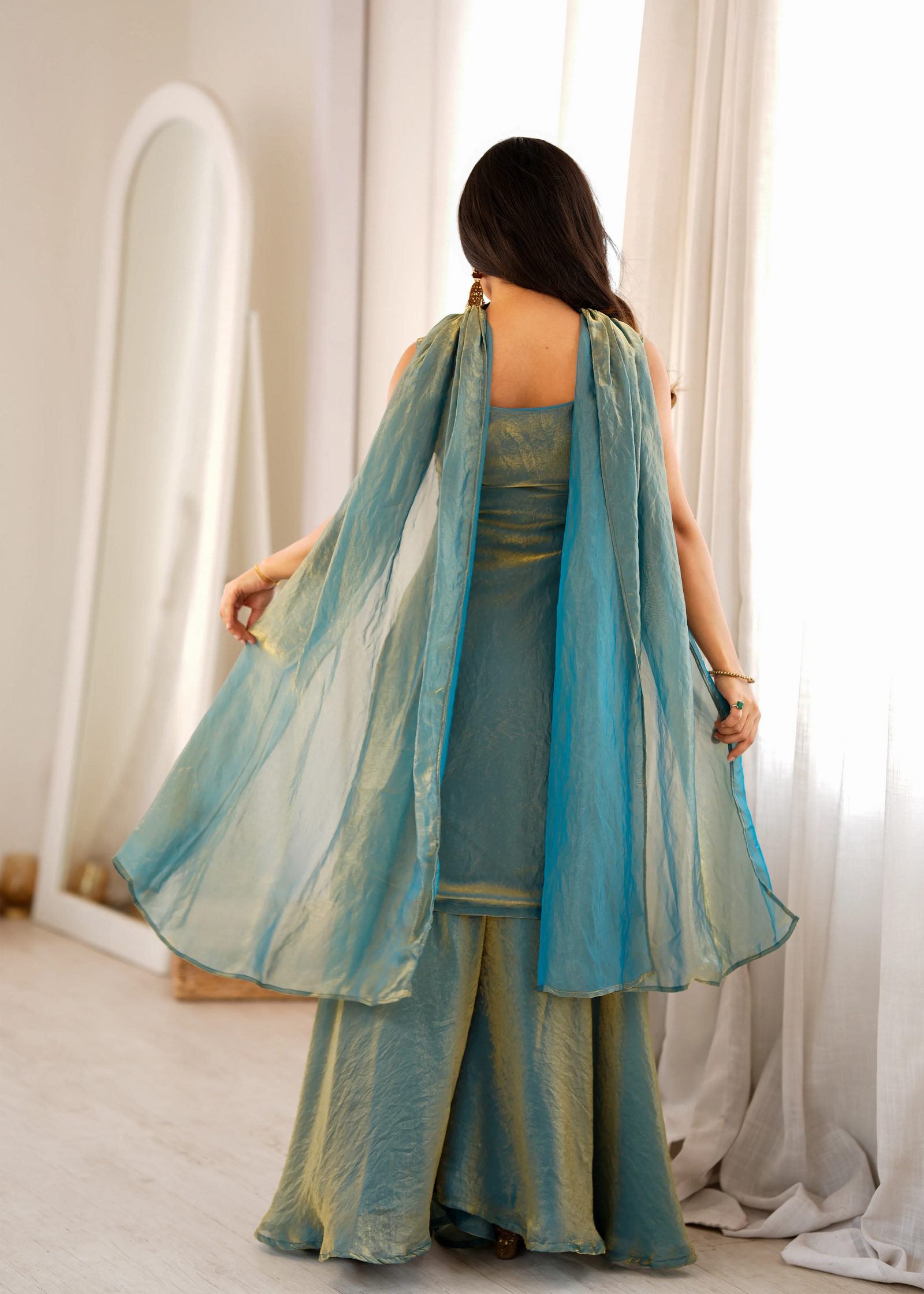 Woman wearing a teal traditional outfit with a matching dupatta in a bright room.