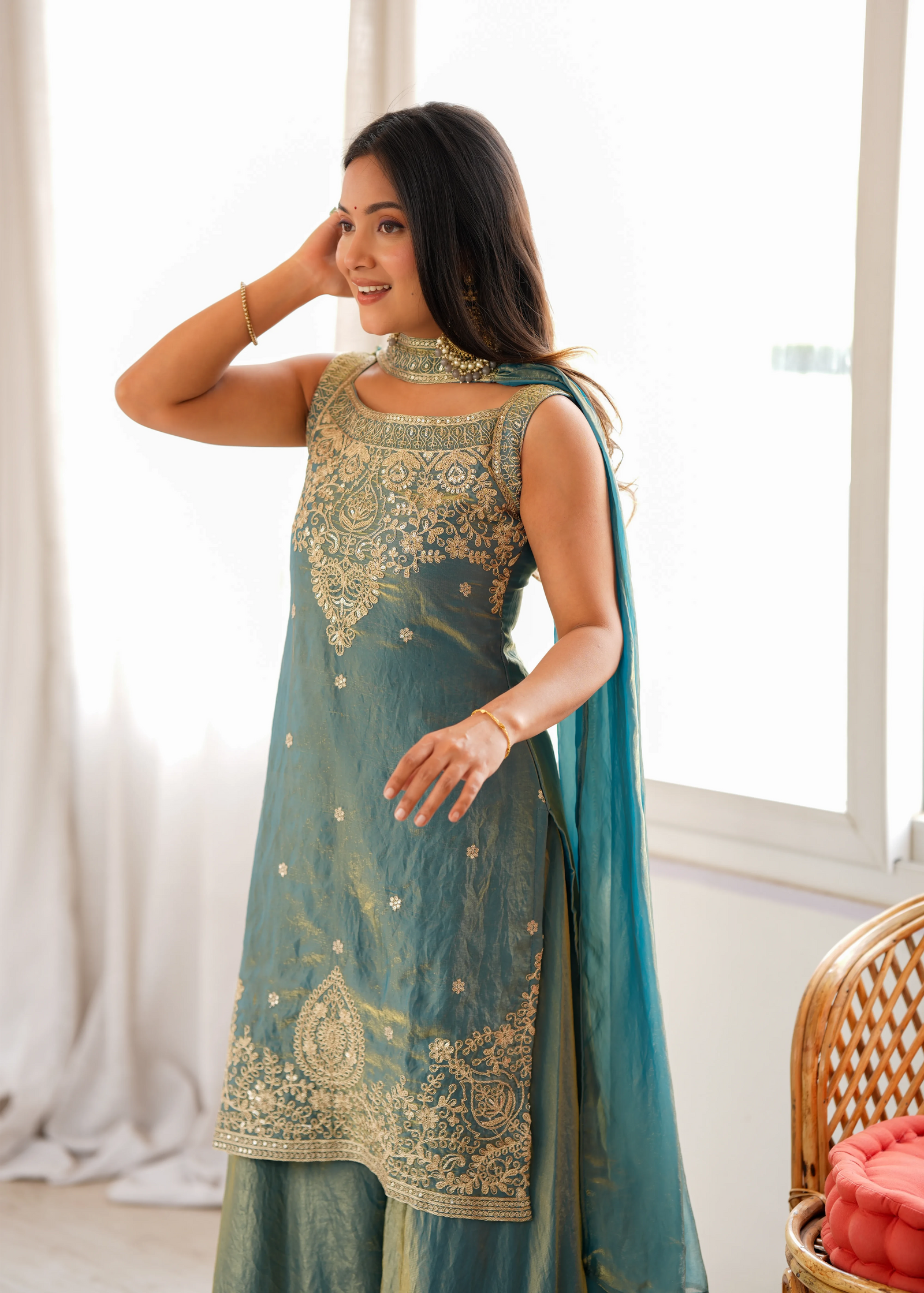Woman wearing a teal and gold embroidered traditional outfit in a bright room.