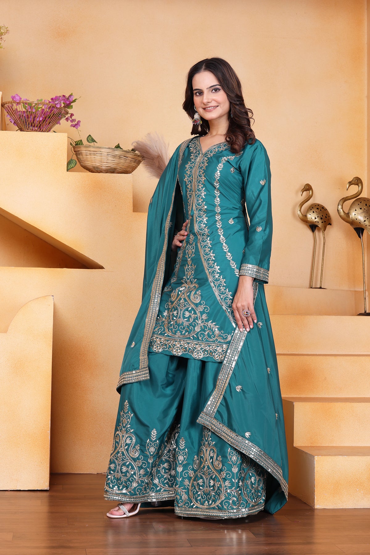 Woman in a teal embroidered traditional outfit standing on a staircase.