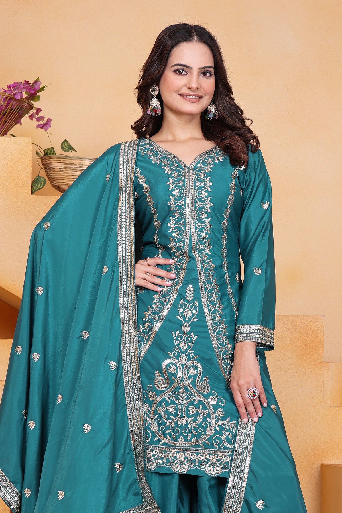 Woman wearing a teal embroidered traditional outfit with a beige background