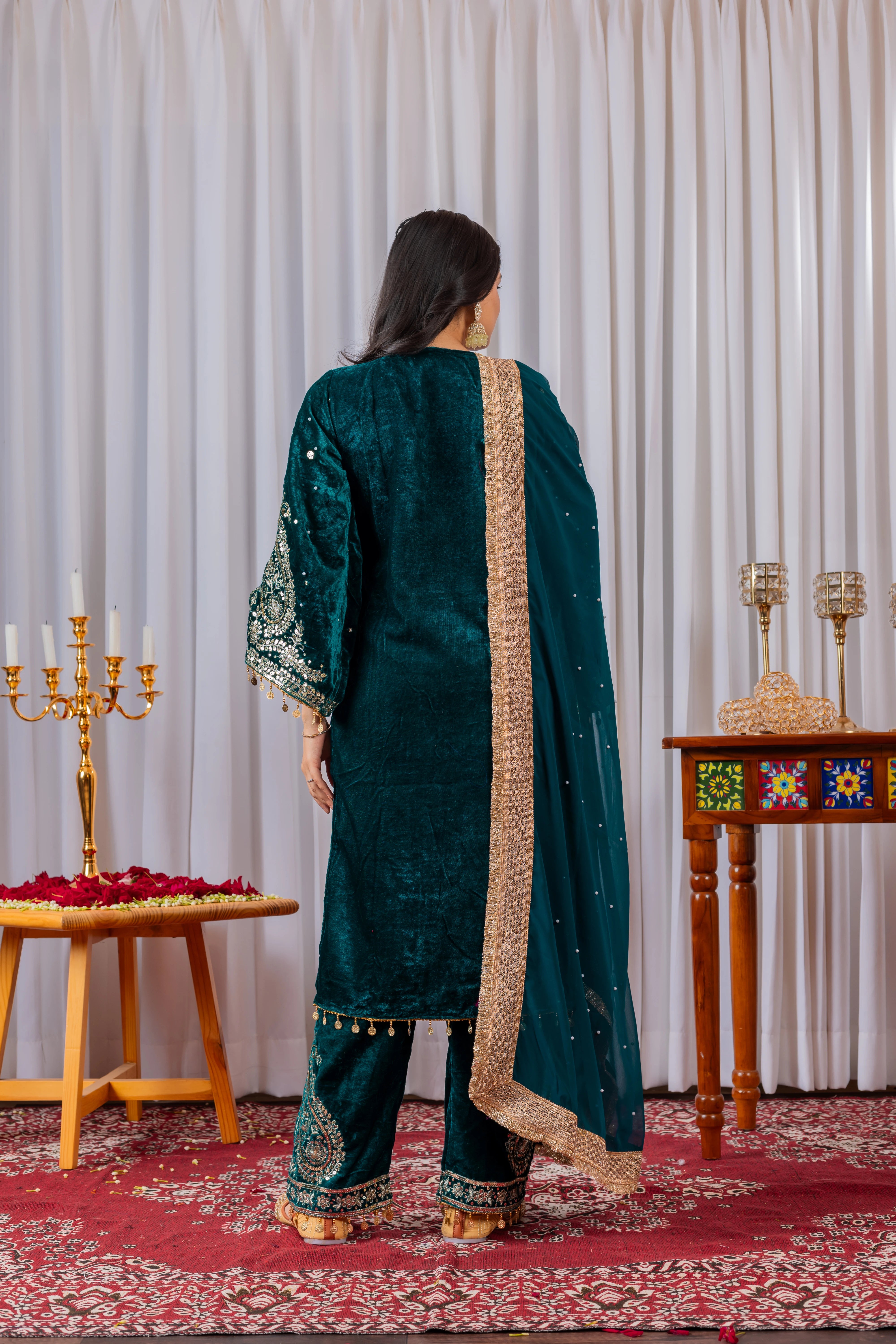 Person wearing a green traditional outfit with gold details in a decorated room.
