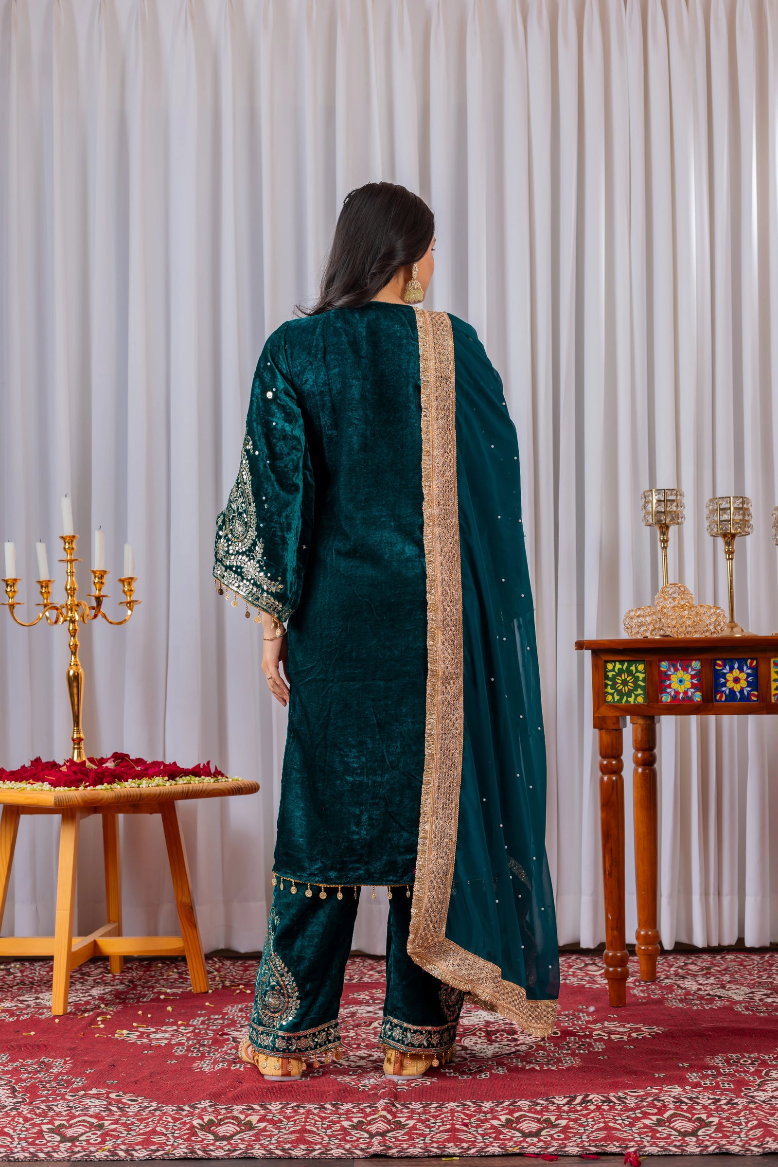 Person wearing a green traditional outfit with gold details in a decorated room.