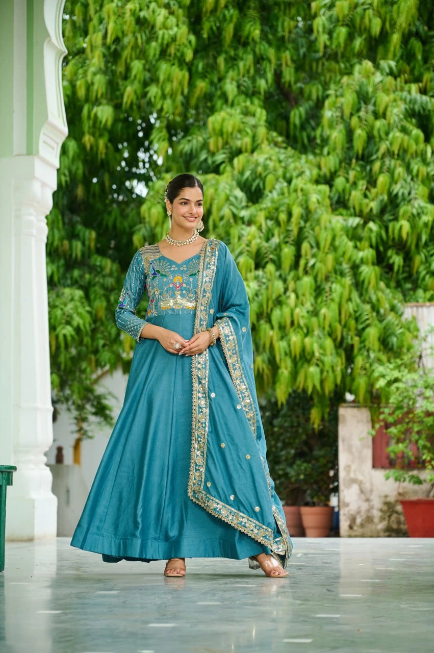 Woman in a blue traditional outfit standing outdoors with greenery in the background