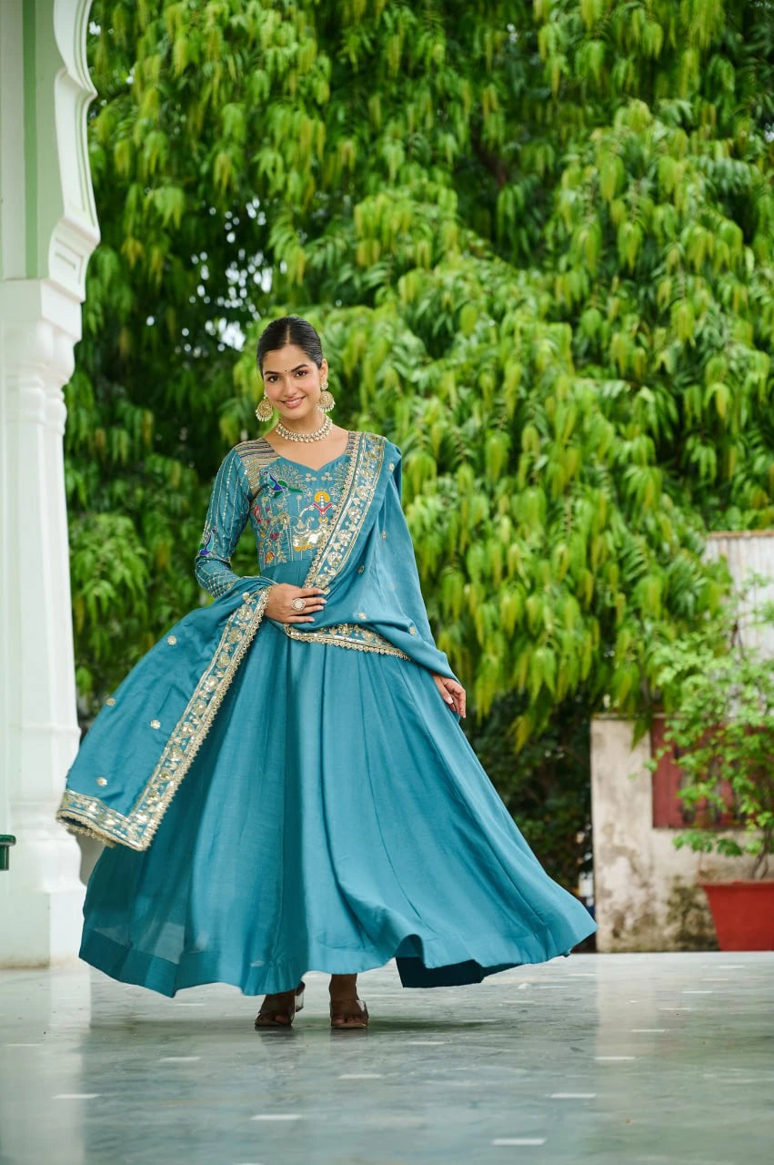 Woman in a blue traditional outfit standing outdoors with greenery in the background