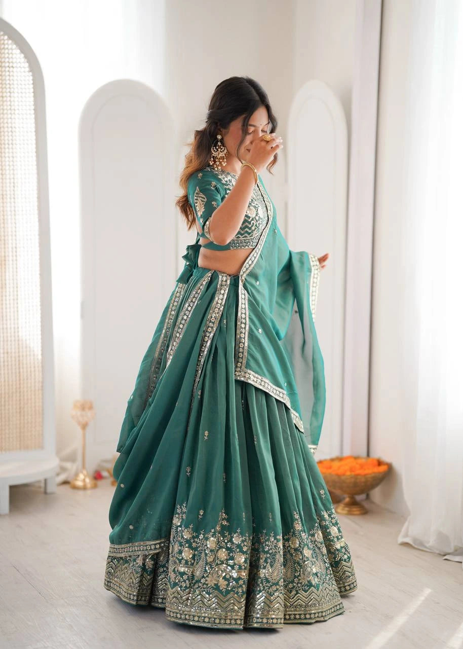 Woman in a teal saree with floral patterns standing in a minimalistic room.