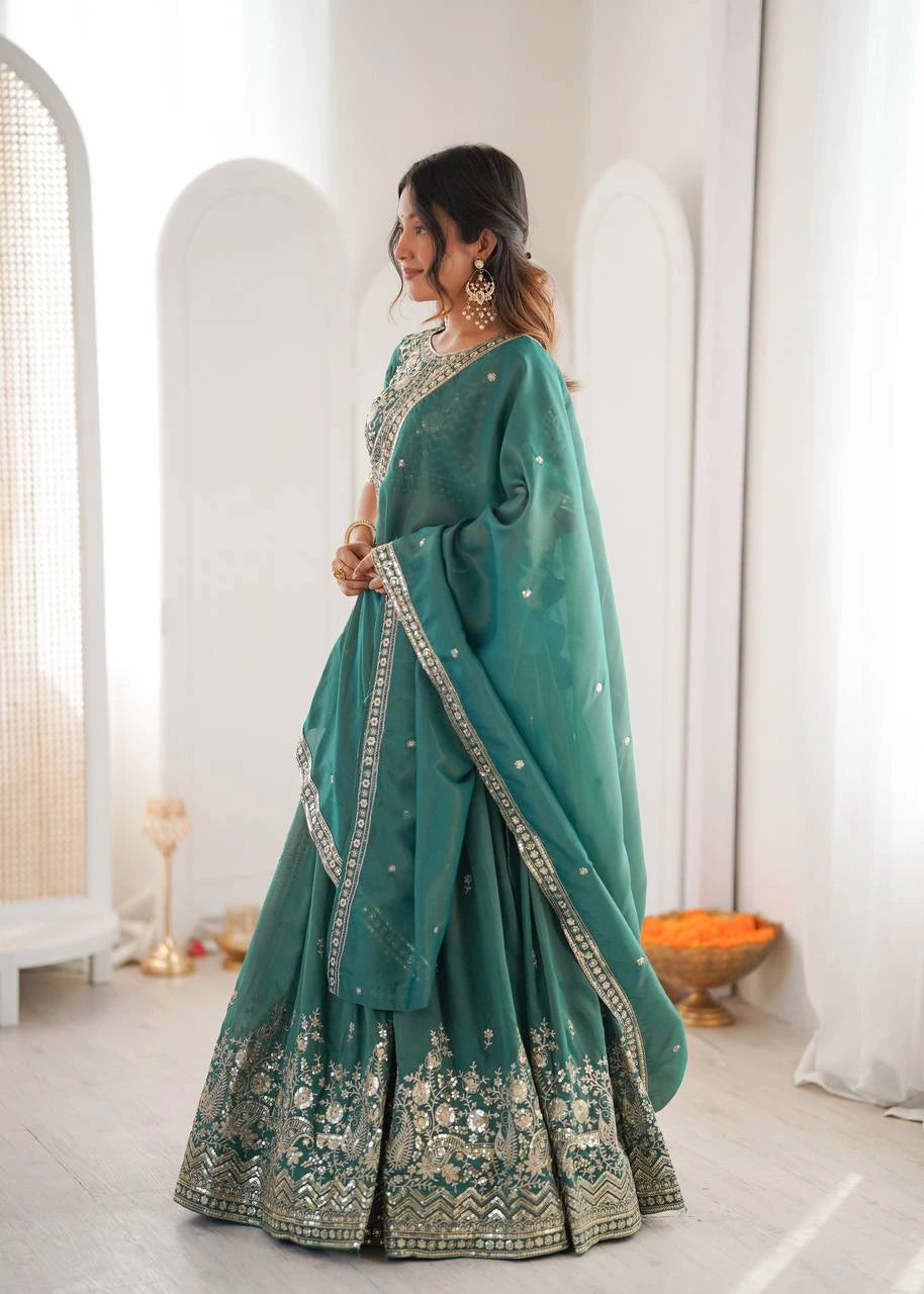 Woman in a teal traditional outfit with intricate patterns in a minimalistic setting.