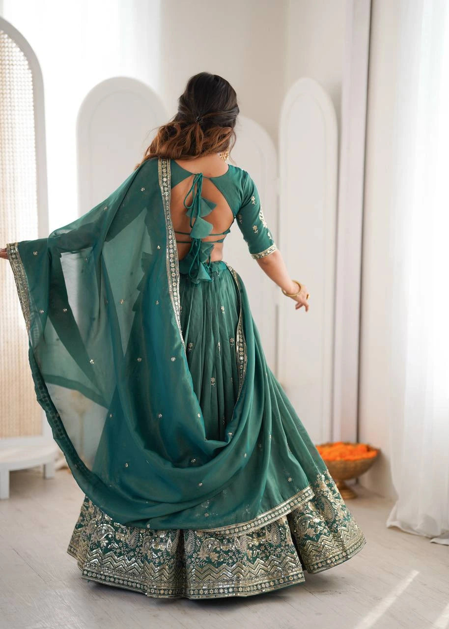 Woman in a green traditional outfit with a sheer dupatta in a minimal indoor setting.