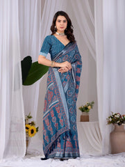 Woman wearing a blue saree with a pattern, standing against a white curtain background.
