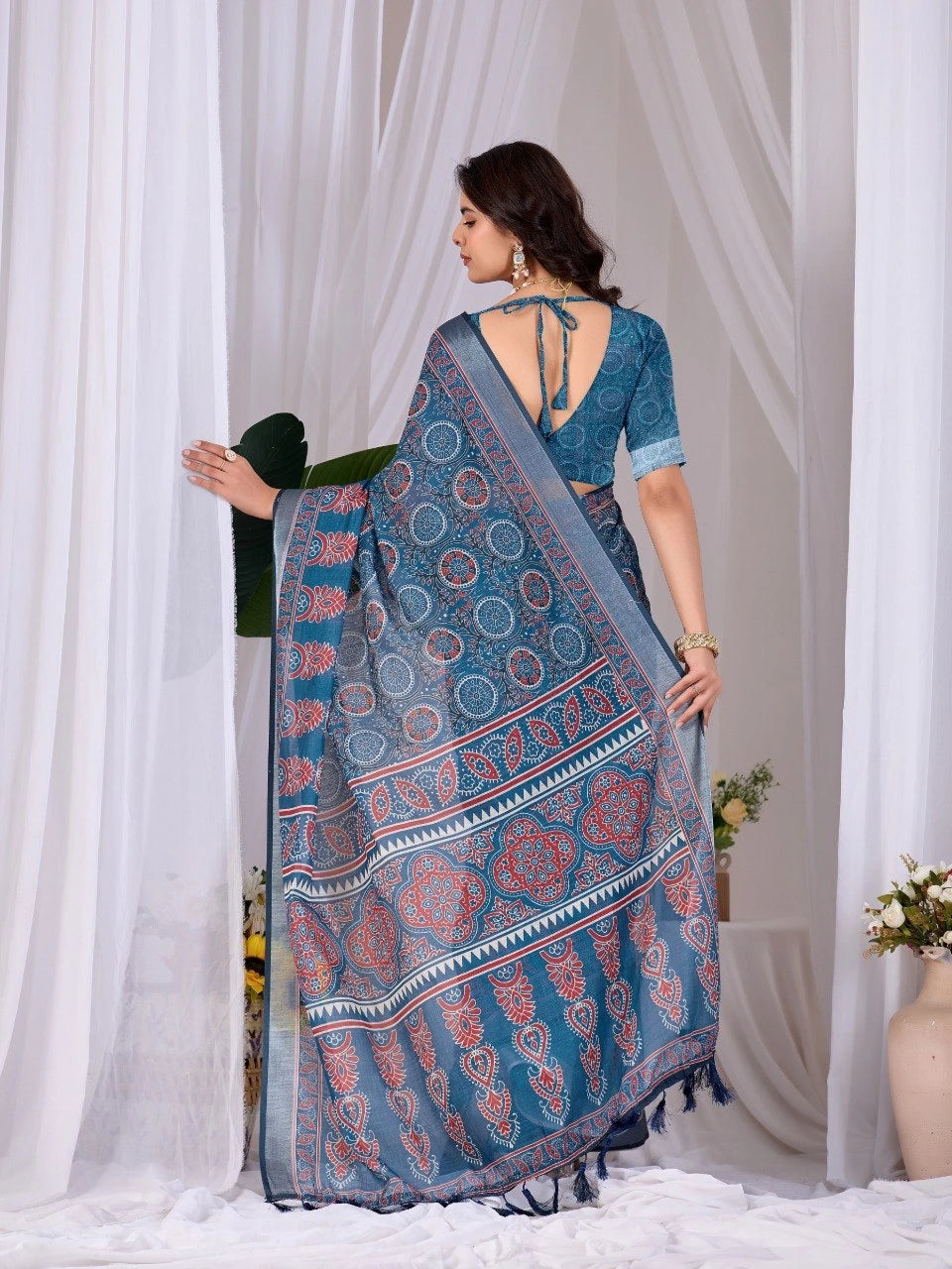 Woman holding a blue patterned saree in front of white curtains