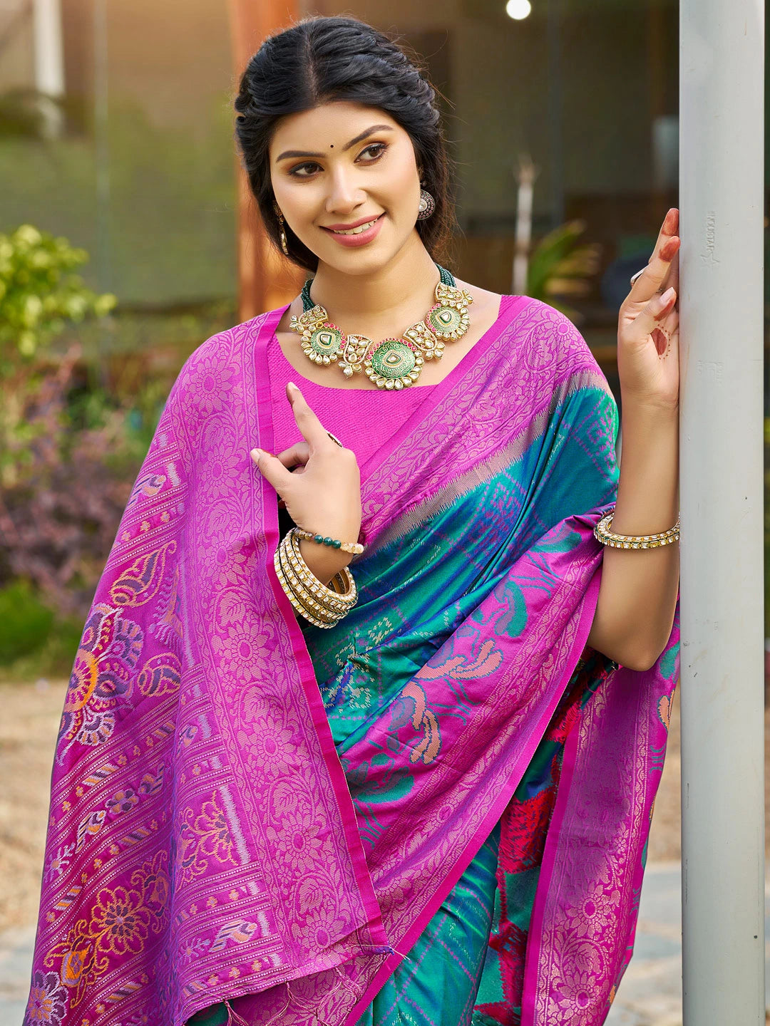 Woman wearing a colorful saree with a vibrant pink and blue pattern, standing outdoors.