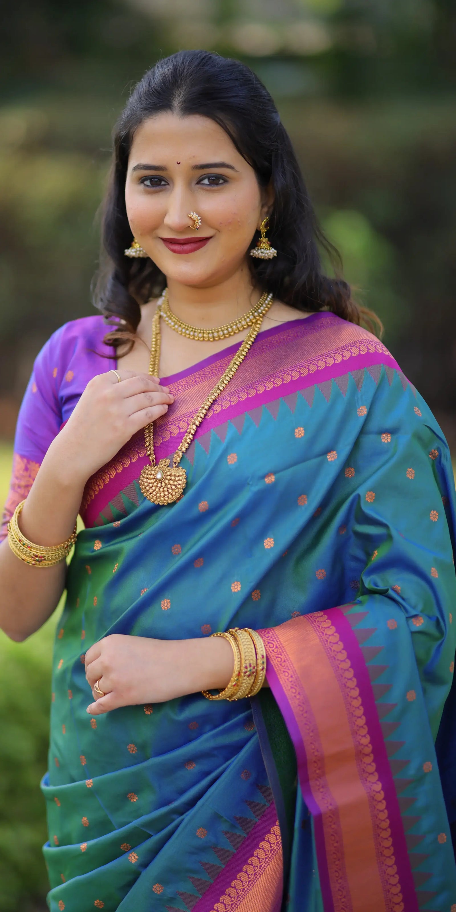 Woman wearing a colorful saree with jewelry against a blurred natural background