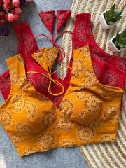 Red and yellow embroidered tops on a textured surface with flowers and plants in the background.