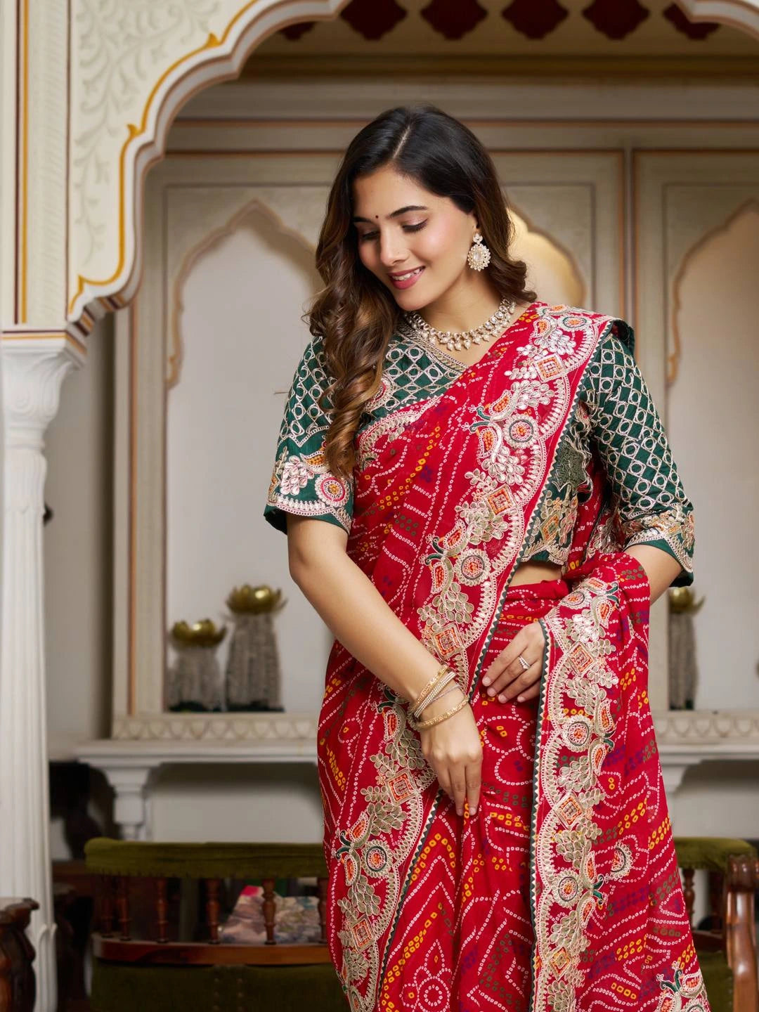 Woman wearing a traditional red and green saree with intricate patterns in an ornate room.
